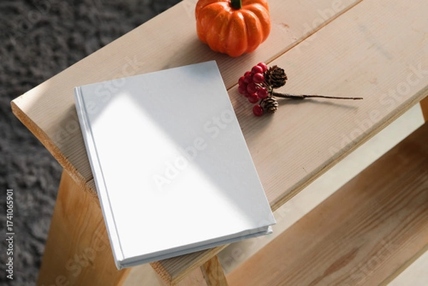 Fototapeta High angle view of white hard cover book on wooden decorative ladder with a pumpkin and red berries
