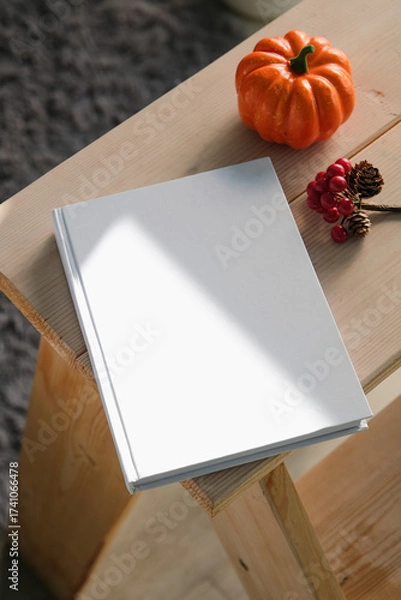 Fototapeta High angle view of white hard cover book on wooden decorative ladder with a pumpkin and red berries