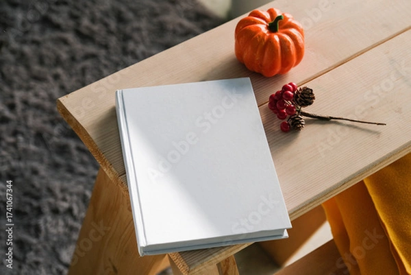 Fototapeta High angle view of white hard cover book on wooden decorative ladder with a pumpkin and red berries
