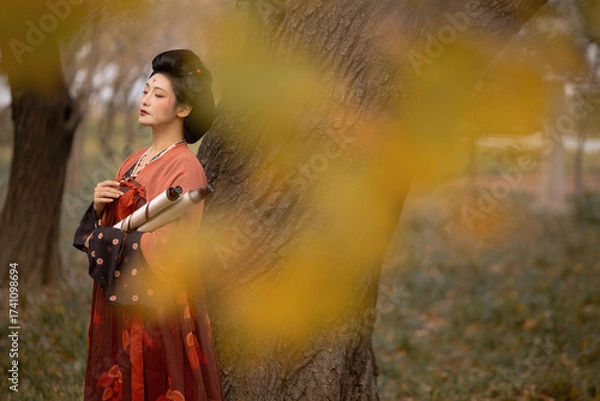 Fototapeta Woman in a red hanfu standing by a tree in an outdoor setting with a serene atmosphere.