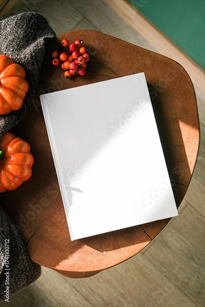 Fototapeta High angle view of white hard cover book on wooden decorative table with a pumpkin and red berries