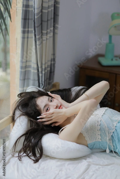 Fototapeta Woman in light blue top relaxing on a bed with soft pillows in a cozy room.
