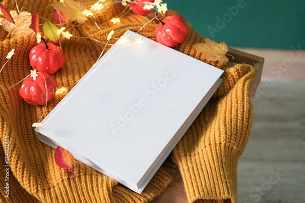 Fototapeta High angle view of white book on wooden decorative table with fairy lights , leaves and yellow sweater