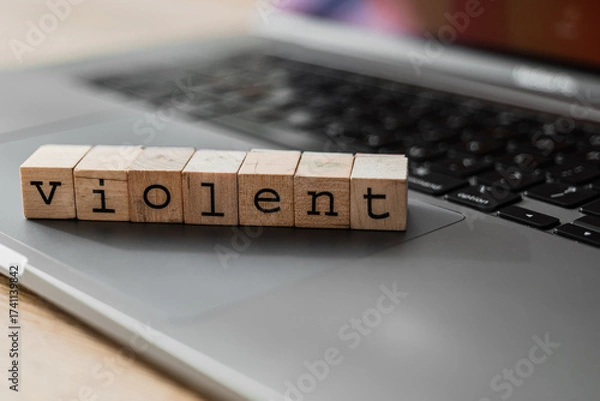Fototapeta Wooden blocks spelling the word VIOLENT on a laptop keyboard, symbolizing online aggression and cyberbullying