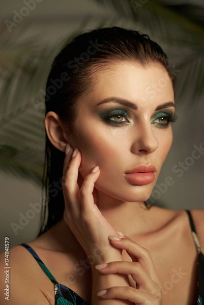 Fototapeta model displays stunning makeup with artistic eyeshadow and flawless skin. She poses gracefully with a thoughtful expression, highlighting her beauty. soft background enhances her features