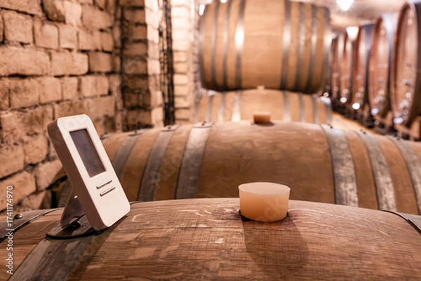 Fototapeta Digital thermometer on an oak barrel measuring precise temperature and humidity for optimal wine aging in a rustic cellar