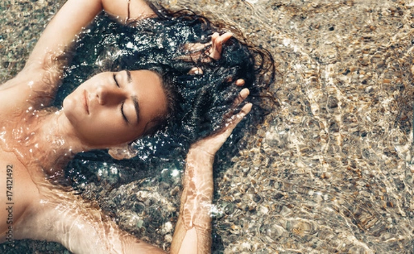 Obraz beautiful young woman lying down in water on the beach