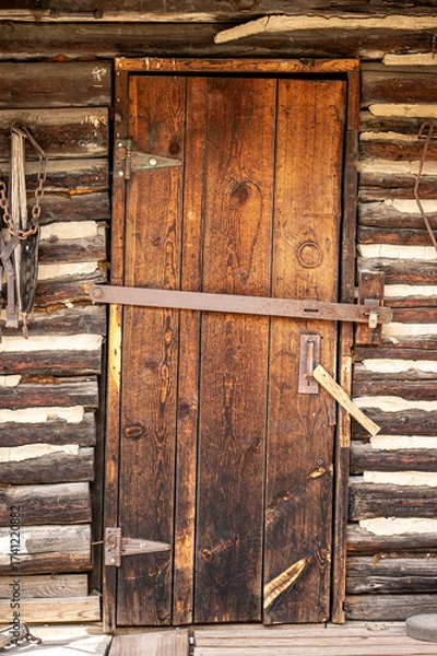 Fototapeta Antique wooden door closed with rustic old mining work tools on the weathered wood wall. Historic house building entrance for architecture background