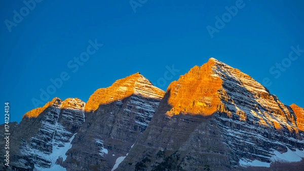 Fototapeta Morning light shines on the mountaintop of Maroon Bells at sunrise against the clear blue sky. Bell-shaped peaks in the Elk mountains. Famous mountain view in Colorado, USA