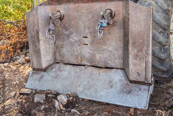 Fototapeta Rusty heavy machinery bucket presenting a face like appearance with hooks for eyes, standing on rough terrain