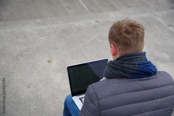 Obraz A young man is sitting and working outside with a laptop