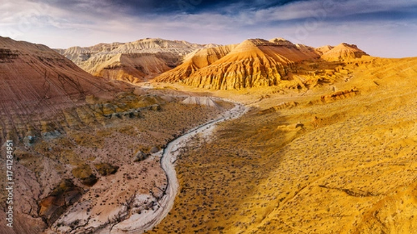 Fototapeta Breathtaking aerial view of colorful mountains and canyons illuminating under dramatic sky in Kazakhstan