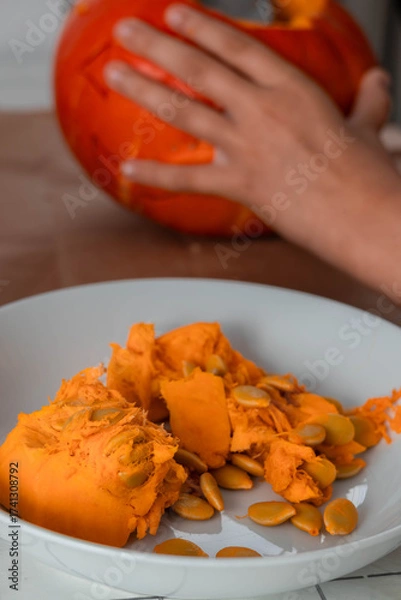 Fototapeta fresh pumpkin flesh in a plate. in the background a child is preparing a pumpkin for Halloween