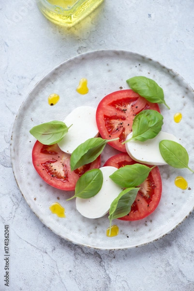 Fototapeta Plate with classic italian caprese salad on a white stone background, vertical shot, high angle view