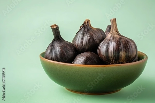 Obraz With a pale green backdrop, a bowl of black garlic bulbs, Generative AI.