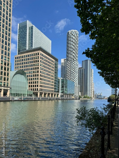 Fototapeta London, UK  Israel, 1 June 2025. A sunny day view of Canary Wharf in London with modern skyscrapers reflected in the water