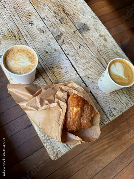 Fototapeta Two cups of latte with heart art and a croissant on a rustic wooden table.