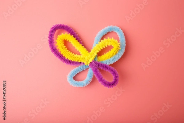 Fototapeta Colorful pipe cleaner butterfly on pink background, ideal for children craft tutorials, preschool education, DIY kits, and playful branding in eco-friendly or creative industries