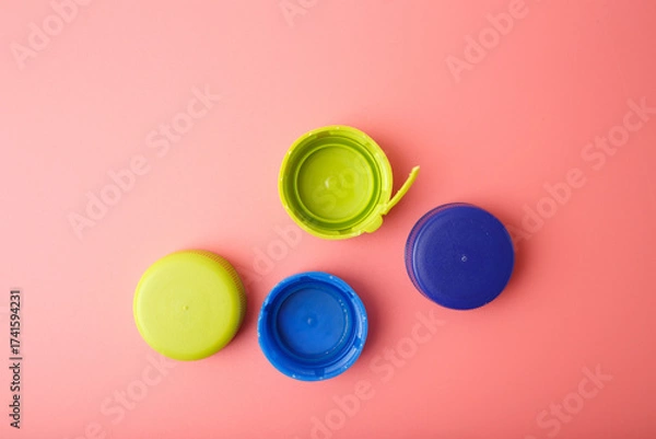 Fototapeta Four plastic caps in varied colors on pink surface, useful for product design, waste management, circular economy visuals, and educational materials on sorting and reuse