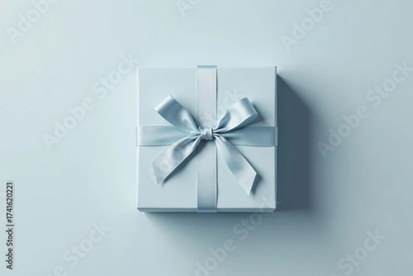 Fototapeta A single light blue gift box with a delicate satin ribbon bow, presented on a matching pastel background
