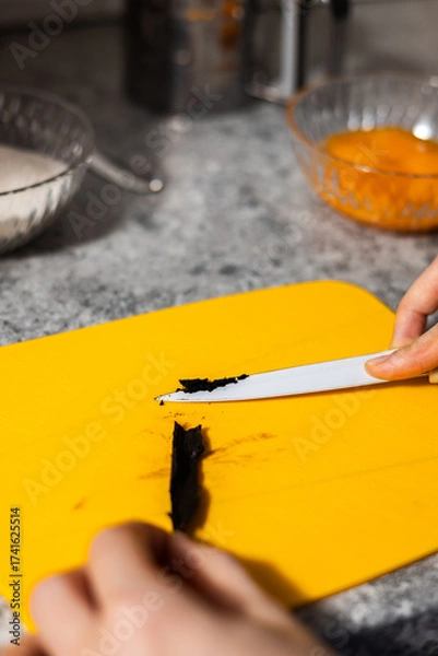 Fototapeta Chef's hands scraping vanilla beans for baking. Close-up on orange cut board.