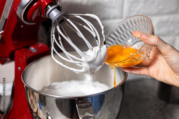 Fototapeta Pastry chef adding agg yolk in the red mixer bowl. Preparing cooking for dinner guests
