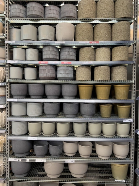 Fototapeta Decorative plant pots of different materials and colors are neatly arranged on metal shelves in a retail store, providing a variety of styles for plant lovers