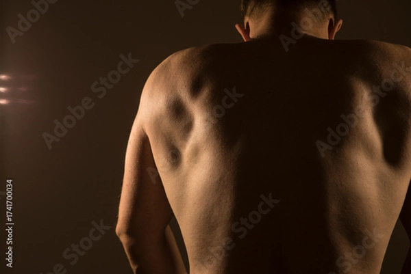 Fototapeta Back view of muscular strong man posing. Sensual. Strong body man. Diet. Photo. Model. Background. Shadow. Sports. 