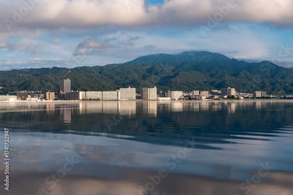 Obraz 早朝の琵琶湖　静かな湖面に湖西のマンション群と背景の比叡山が映る風景　滋賀県大津市