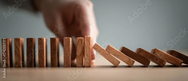 Obraz The Wooden Dominoes Falling as a Hand Stops the Chain Reaction