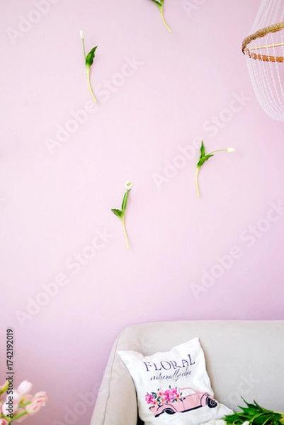 Fototapeta Floral decorative elements arranged on a pastel pink wall, with a cozy couch and a stylish pillow, creating a serene and inviting interior design atmosphere