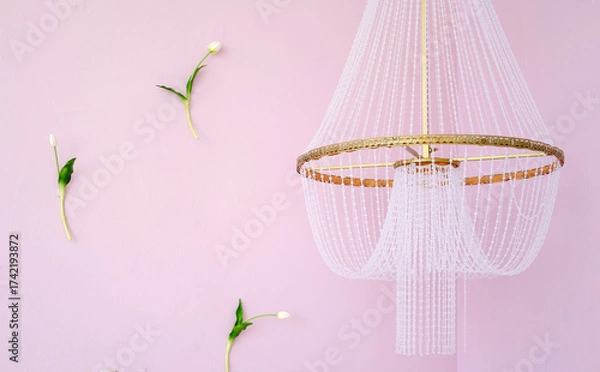Fototapeta Elegant chandelier with delicate beadwork hangs from ceiling against soft pink wall, surrounded by minimalistic floral accents, creating a serene and stylish atmosphere. Copy space