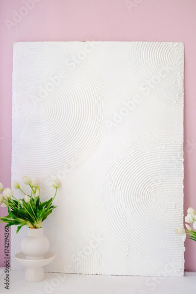 Fototapeta Textured white wall art with circular patterns, complemented by a minimalist vase of fresh flowers, creating a serene and stylish interior decor atmosphere. Copy space