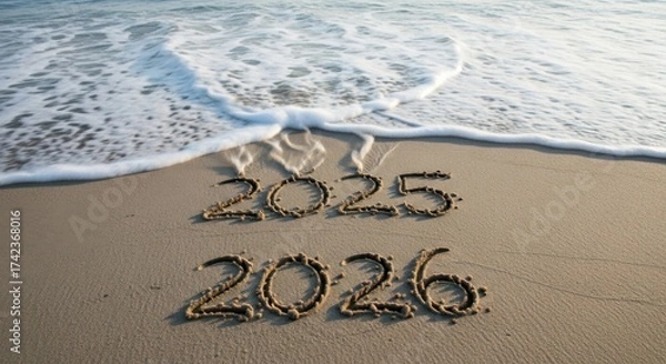 Fototapeta The years 2025 and 2026 written in the sand on a beach near the ocean