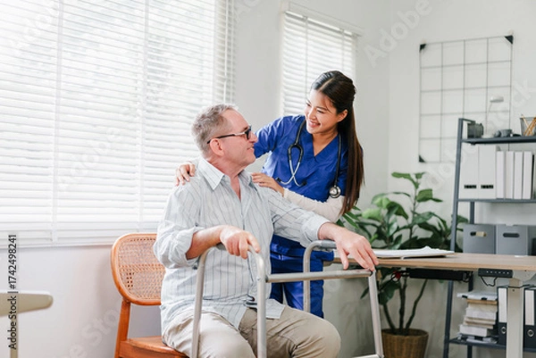 Fototapeta Elderly man with walker and smiling nurse providing supportive care in bright home office setting, warm compassionate interaction