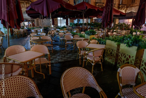 Fototapeta Nighttime Outdoor Cafe with Wicker Bistro Chairs and Maroon Umbrellas