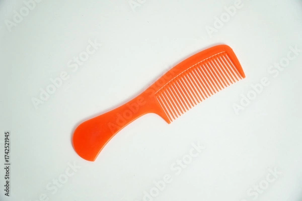 Fototapeta A bright orange plastic comb is isolated on a clean white background. Its vibrant color and simple design make it perfect for concepts of hair care, beauty, or grooming accessories.

