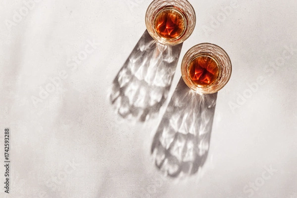 Fototapeta Whiskey Glasses with Shadows and sunlight Reflection on beige background,neutral photo minimal style, aesthetic top view summer still life, refraction throug crystal shine cups, caustics