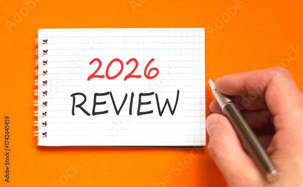 Fototapeta 2026 Review symbol. Concept words 2026 Review on beautiful white note. Beautiful orange paper background. Businessman's hand with pen. Business and 2026 review concept. Copy space.