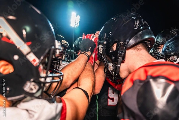 Fototapeta American football players huddling, showing teamwork and motivation