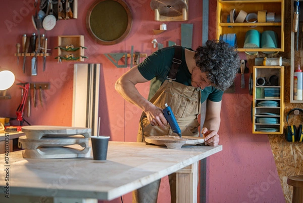Fototapeta Woodworker apply melted silicone along edges of imperfections in crafted timber before resin repair. Crack stabilization, wood surface defect correction, furniture flaw preventive wood restore