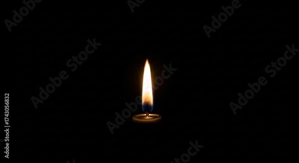 Fototapeta A single candle flame burns brightly against a stark black background casting a warm glow