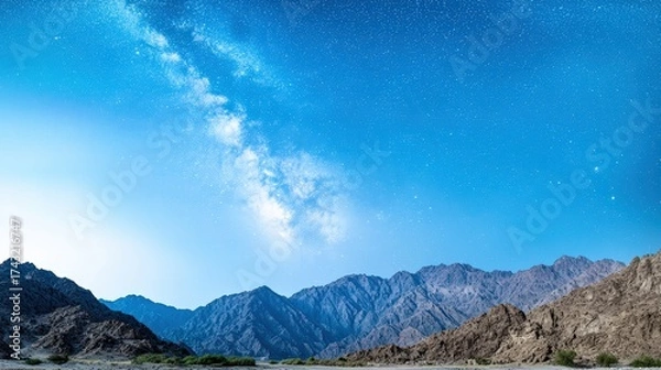 Fototapeta A breathtaking view of rugged mountain peaks illuminated by a vibrant starry sky, showcasing the Milky Way cascading across the night. The serene landscape contrasts with the vastness of the