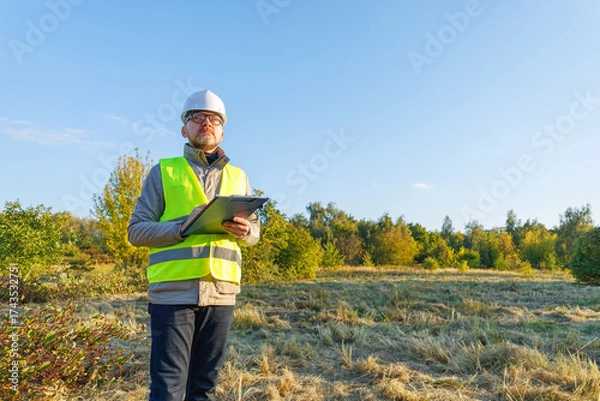 Fototapeta Male engineer inspects the condition of a new construction site. Work forestry inspector, environmental control. Ecologist conducts environmental monitoring soil analysis. 