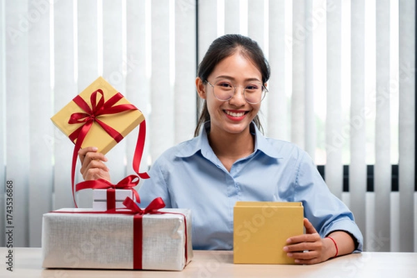 Obraz Happy woman is smiling and holding present box to wrapped with red ribbon while preparing gift for celebrate