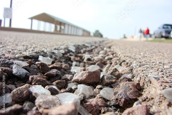 Fototapeta Road edge with loose rocks, shelter in the background, bright day