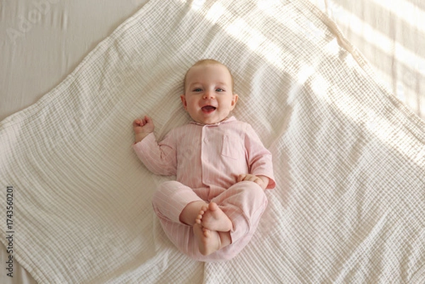 Fototapeta Top view shot of a joyful baby wearing pink pajamas lying on the back and laughing. Copy space, background.