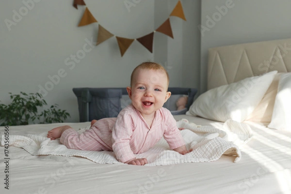 Fototapeta Playful baby learning to crawl on the bed. Copy space, background.