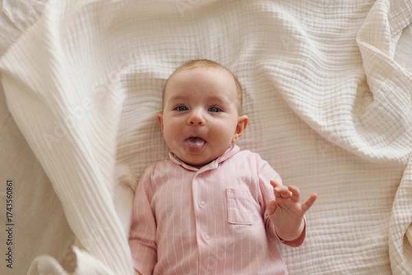 Fototapeta Top view shot of a joyful baby wearing pink pajamas lying on the back and laughing. Copy space, background.