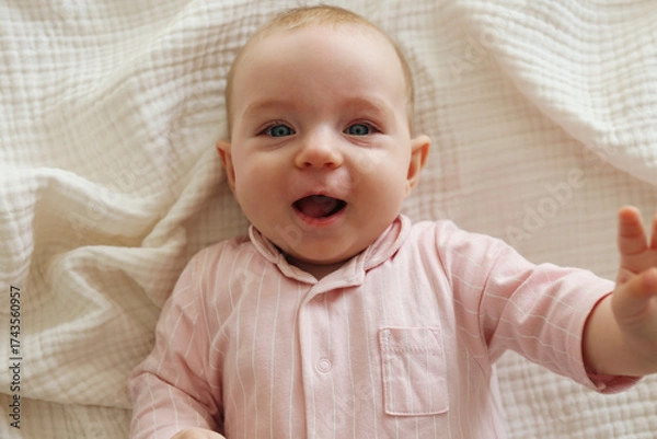 Fototapeta Top view shot of a joyful baby wearing pink pajamas lying on the back and laughing. Copy space, background.
